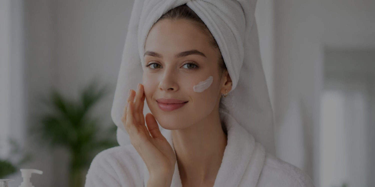 Woman applying cream to her face with a towel on her head in a bathroom setting