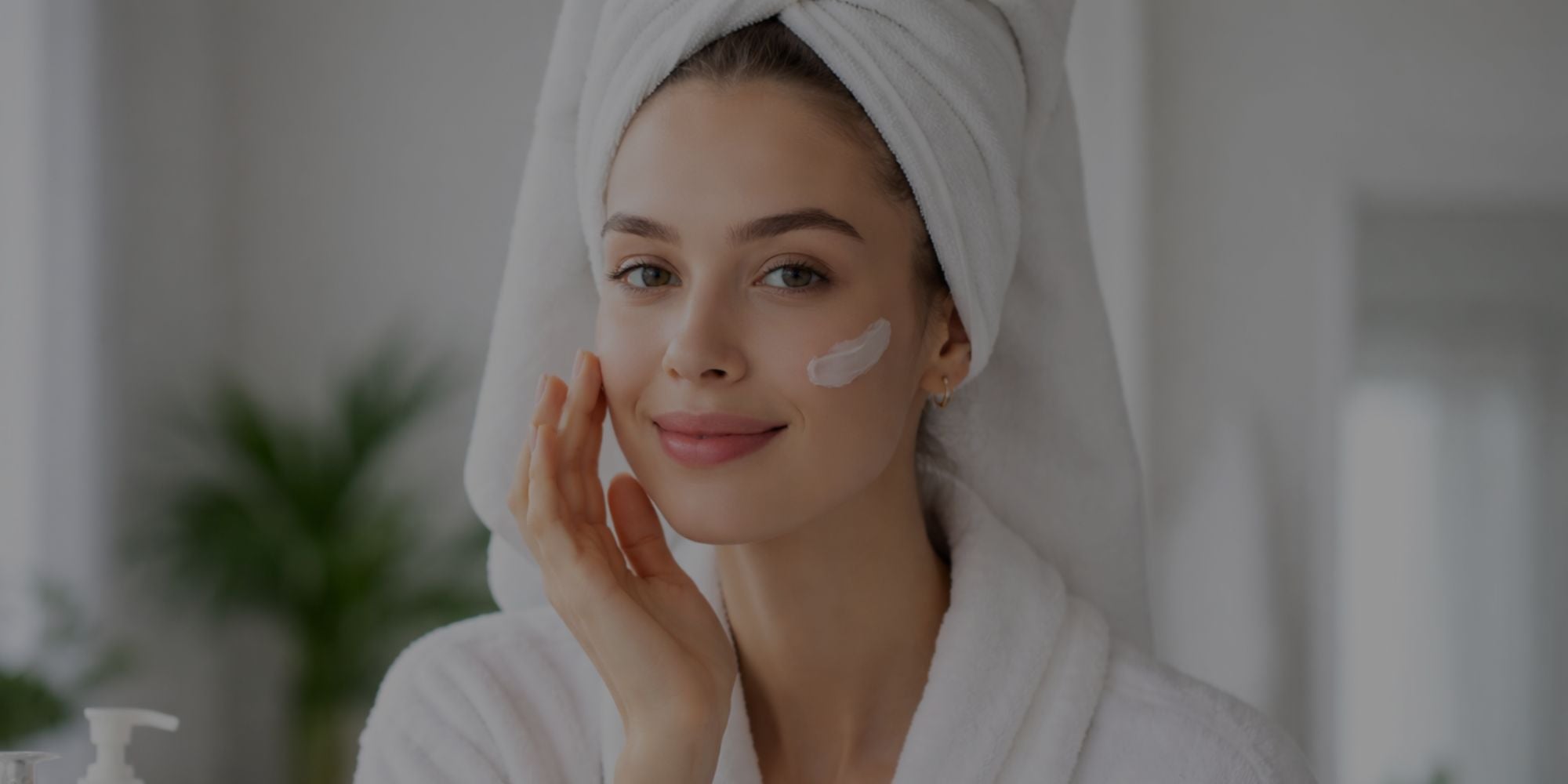 Woman applying cream to her face with a towel on her head in a bathroom setting