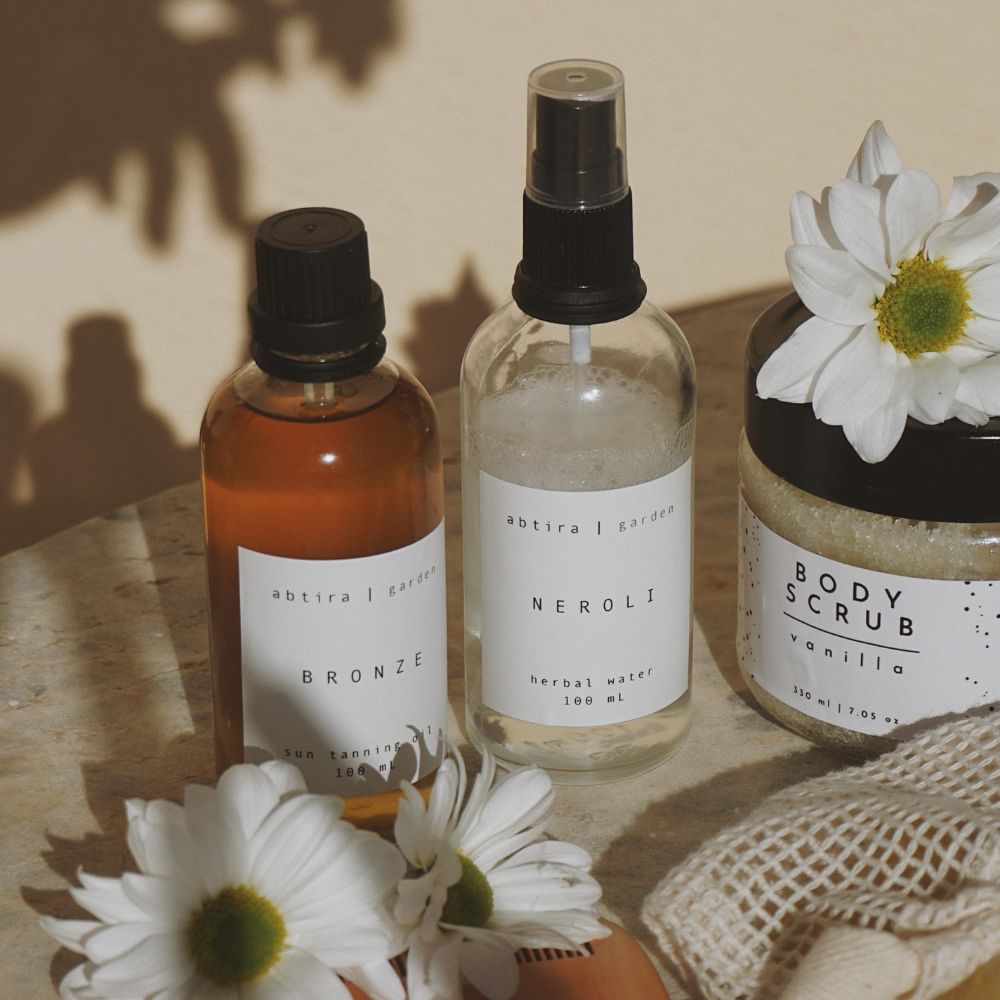Three skincare products with labels and flowers on a wooden surface