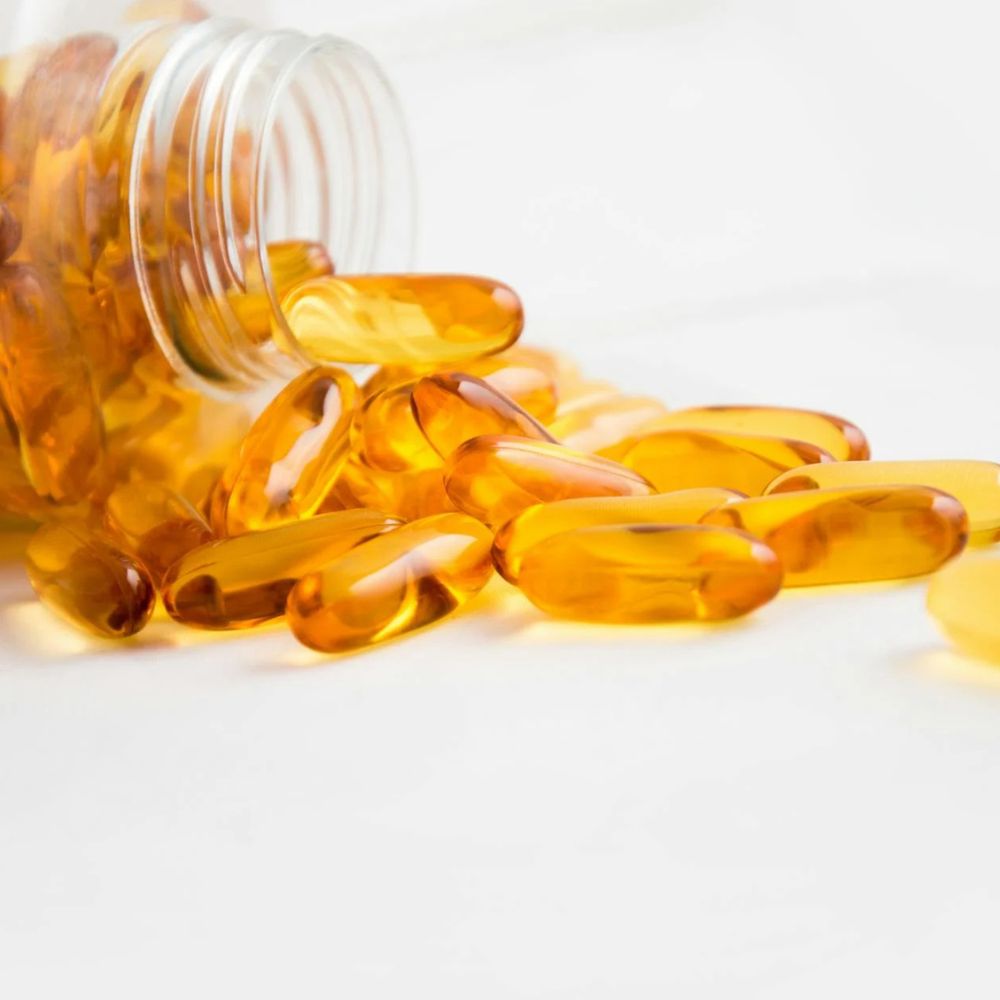 Yellow capsules spilling out of a glass bottle on a white background